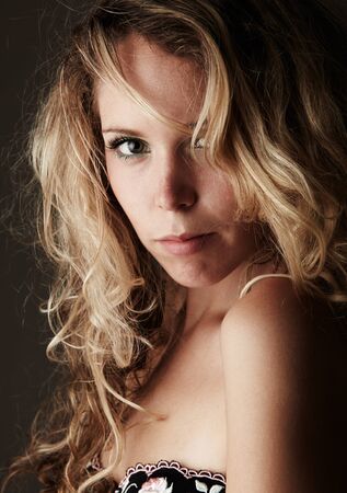 Beautiful young blonde caucasian woman with long curly honey blonde hair in black embroidered lingerie on a neutral backgroundの写真素材
