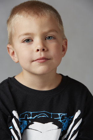 5 year old caucasian boy with short blonde hair, blue eyes and a light, healthy complexion wearing a long sleeve t-shirt. Shot in studio on a grey background.の写真素材