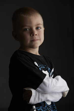 5 year old caucasian boy with short blonde hair, blue eyes and a light, healthy complexion wearing a long sleeve t-shirt. Shot in studio on a dark grey background.の写真素材