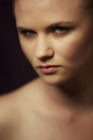 Portrait of a serious young adult caucasian nude woman with a ire expression on her face. Blonde hair in a ponytail with neutral, natural makeup - Shallow Depth of Field, Focus on Front Eyeの写真素材