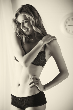 Sexy and beautiful young adult caucasian blonde woman in black lingerie in a light white bedroomの写真素材