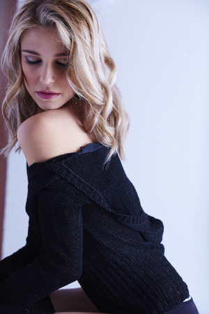 Sexy and beautiful young adult caucasian woman in black lingerie and a knitted see through hoodie in a light white bedroomの写真素材