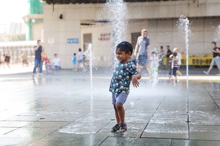 happy kid playing with fountain in front of buildingのeditorial素材