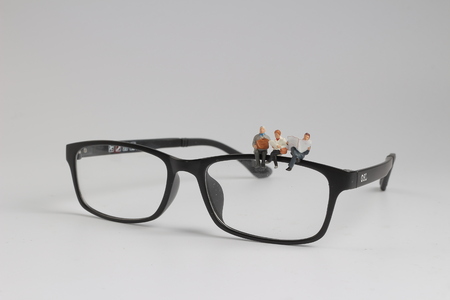 a min figure sitting and reading newspaper on glasses.の写真素材