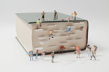 a miniature people mini figures with backpack walking and climbing on a mountain of textbooksの写真素材