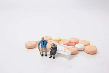 an Elderly figure sitting on a pile of white pills.の写真素材
