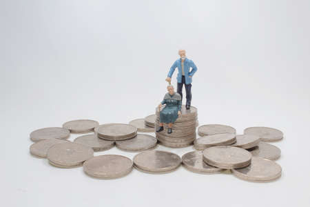 mini people elderly sitting on stack coinsの写真素材