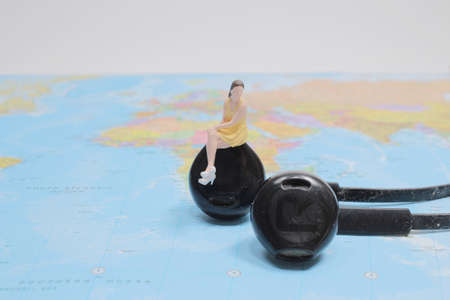 figure sitting on white earphone on world map.