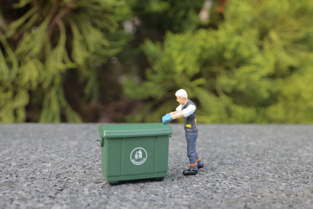 Worker of cleaning company in orange uniform with a green garbage binの写真素材
