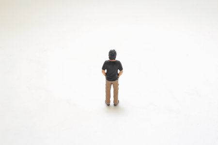 lone miniature figurine of a man stands casually against a plain white backdropの写真素材