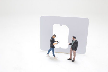 miniature figures are engaged in conversation with a large SIM card in the backgroundの写真素材