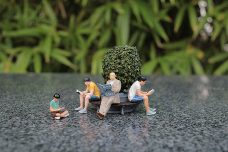 Tiny figures sit on a bench, engaged in reading, surrounded by greeneryの写真素材