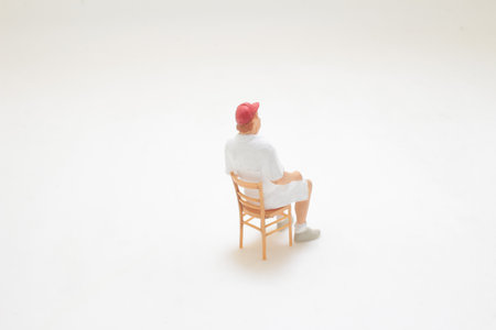 A small-scale figurine depicting a man seated on a chair, isolated