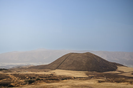 A serene view of a large brown hill surrounded by open fieldsの写真素材