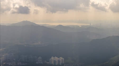 mountains in the foreground with a coastal city and vivid cloudy sky in the distance.の写真素材