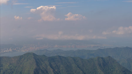 mountains in the foreground with a coastal city and vivid cloudy sky in the distance.の写真素材
