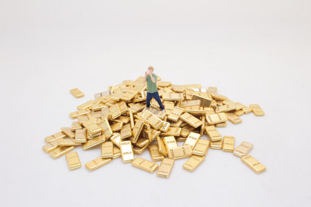 A figurine of a person stands amidst a collection of gold barの写真素材