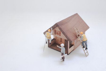 Miniature figurines collaborating on constructing two wooden house-shaped model