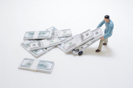 figurine is seen moving bundles of currency on a miniature hand truckの写真素材