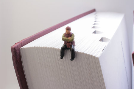 concept showcasing a miniature figurine sitting on the edge of an open bookの写真素材