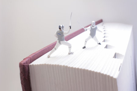 Miniature fencing figures duel atop a thick book, symbolizing creativity,の写真素材