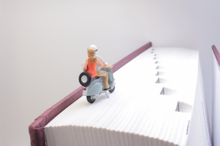 A close-up of a miniature figure riding a vintage scooter placed on a large book.の写真素材