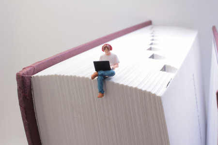 creative concept of a small figure sitting with a laptop on a big book