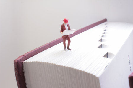 A miniature figure of a worker wearing a hard hat stands on a thick bookの写真素材