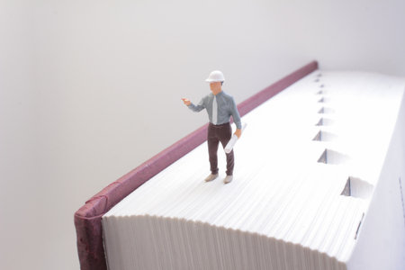 A conceptual photograph featuring a small engineer figure on a massive bookの写真素材
