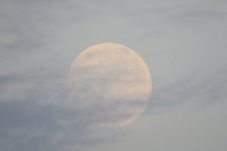 A dreamy image of a full moon partially covered by soft clouds, s