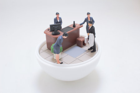 A playful miniature office scene shows a desk setup with tiny figures i