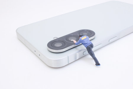 A miniature figure appears to push the triple camera lens on a sleek silver