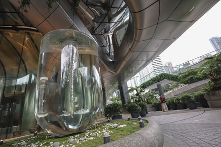 A tall glass water column fountain stands in a modern urban courtyard,のeditorial素材