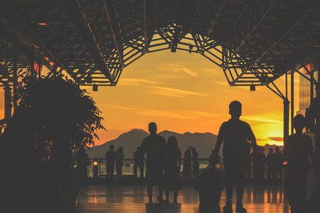 Golden sunset lights a glass walkway where groups stand and walkのeditorial素材