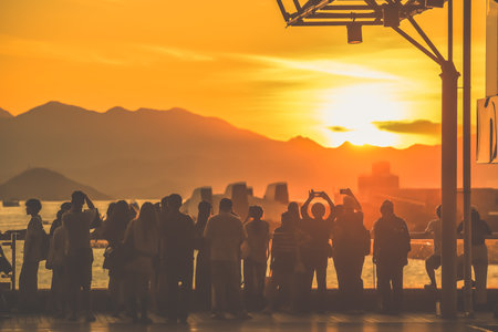 A group of people stands along a waterfront at sunset, capturing