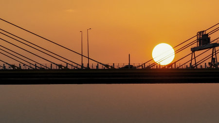 A dramatic sunset casts warm orange light over a city bridge