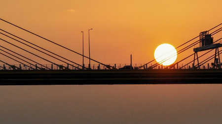 A dramatic sunset casts warm orange light over a city bridgeの写真素材