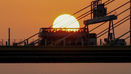 A dramatic sunset casts warm orange light over a city bridgeの写真素材