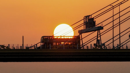 A dramatic sunset casts warm orange light over a city bridgeの写真素材
