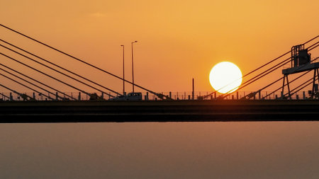 A dramatic sunset casts warm orange light over a city bridgeの写真素材