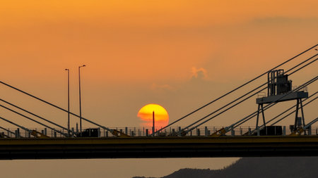 A dramatic sunset casts warm orange light over a city bridge