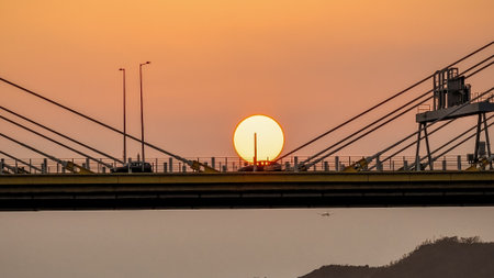 A dramatic sunset casts warm orange light over a city bridgeの写真素材