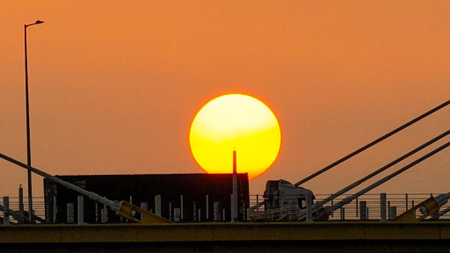 A warm sunset behind a cable-stayed bridge creates striking silhouettesの写真素材