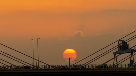 A dramatic sunset casts warm orange light over a city bridgeの写真素材
