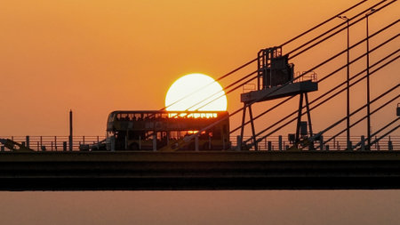 A dramatic sunset casts warm orange light over a city bridgeの写真素材
