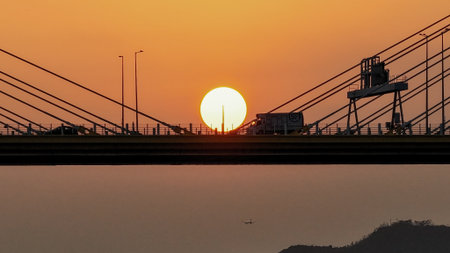 Bridge silhouettes frame a glowing sunset over calm water, w