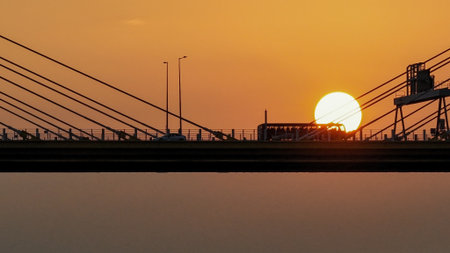 A dramatic sunset casts warm orange light over a city bridgeの写真素材