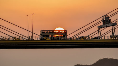 A dramatic sunset casts warm orange light over a city bridgeの写真素材