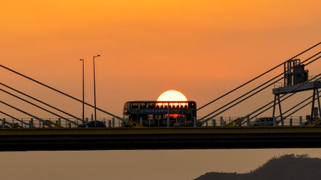 A dramatic sunset casts warm orange light over a city bridgeの写真素材