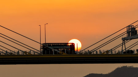 A dramatic sunset casts warm orange light over a city bridgeの写真素材